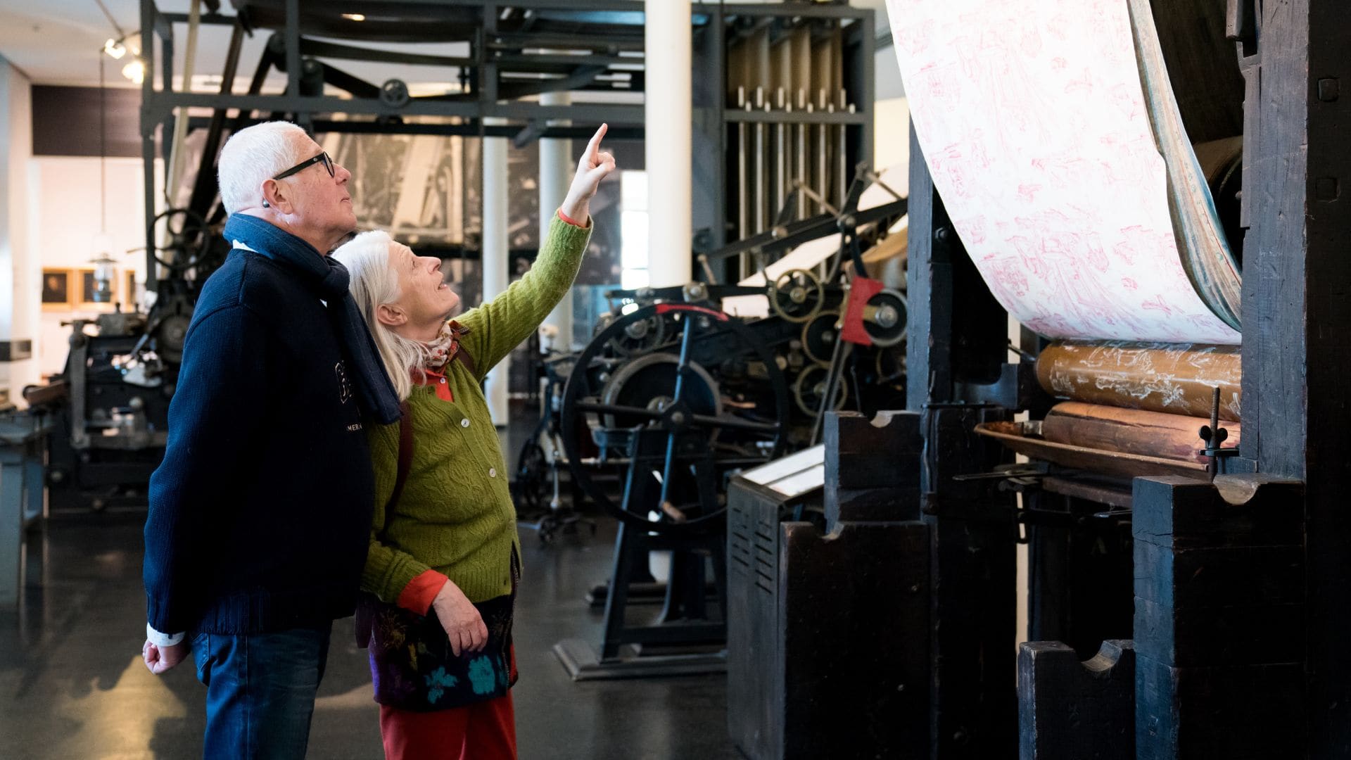 Un couple de seniors observe une impression sur étoffes sur une machine du Musée de l'Impression sur étoffes