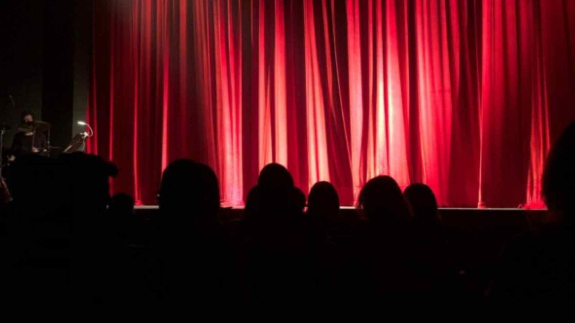 Public assis devant une scène avec des rideaux rouges, attend que le spectacle démarre