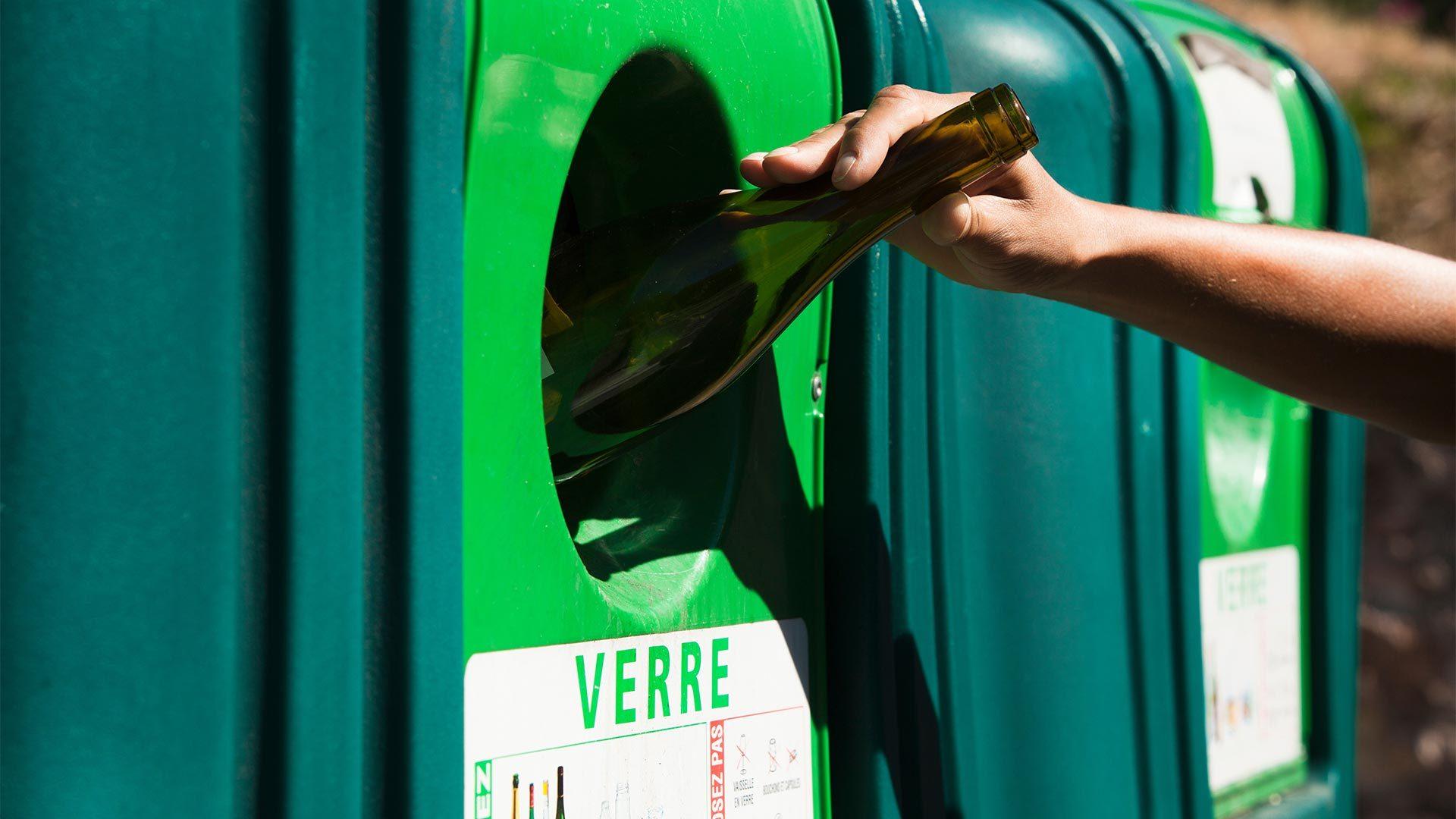 Personne qui dépose une bouteille en verre dans un bac de tri