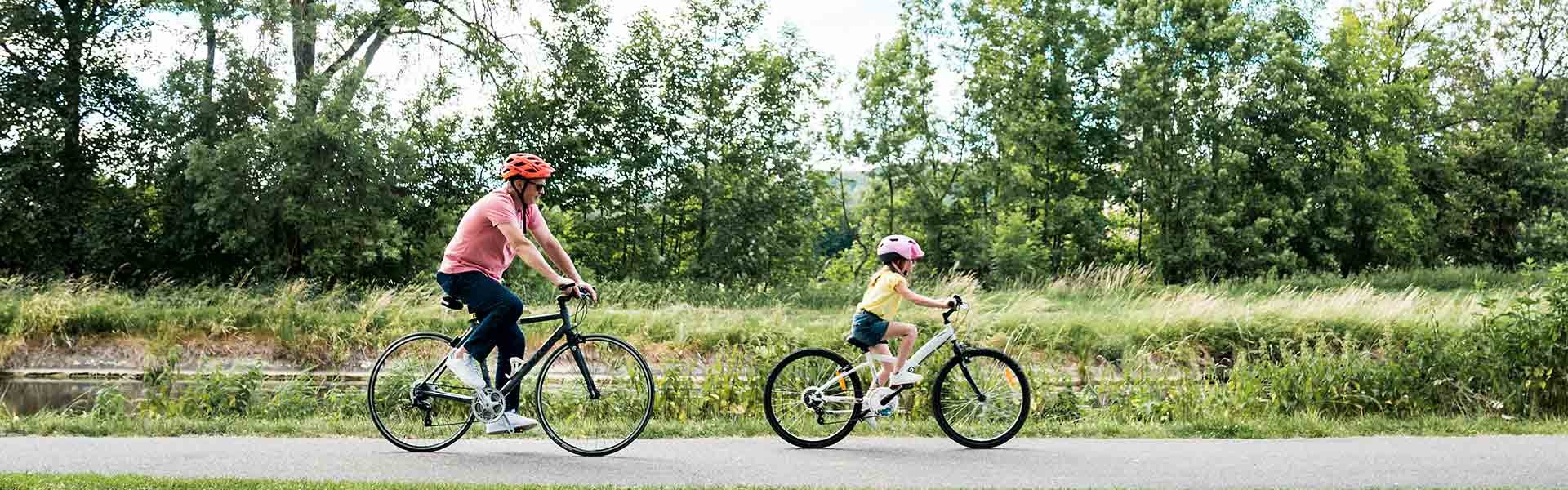 Un enfant et un adulte font du vélo sur une piste cyclable qui borde la nature